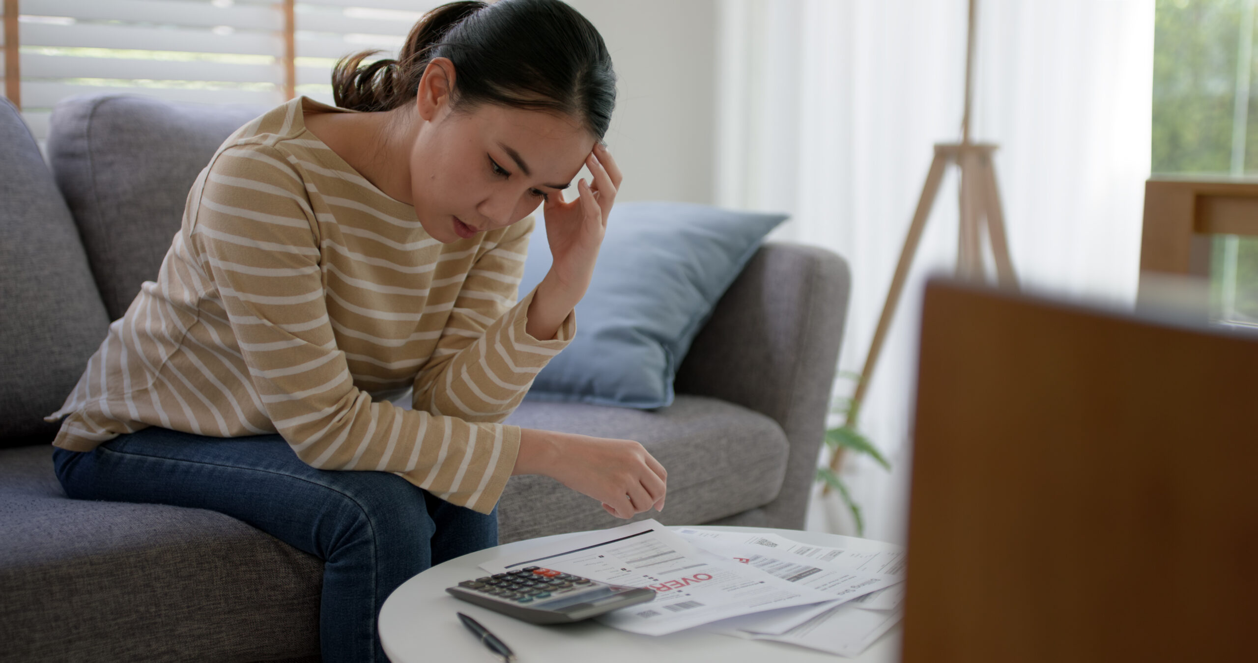 Upset tired young asia sad lady people sit sofa couch at home think hard worry in tax expense saving issue past due loan late payment on covid impact life feel grief pensive struggle in money lost.