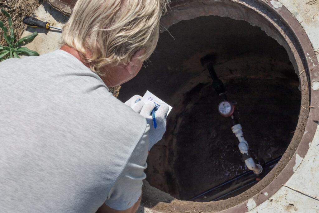 The man bent over the water well and records the readings of the water meter. Checking and fixing the counter
